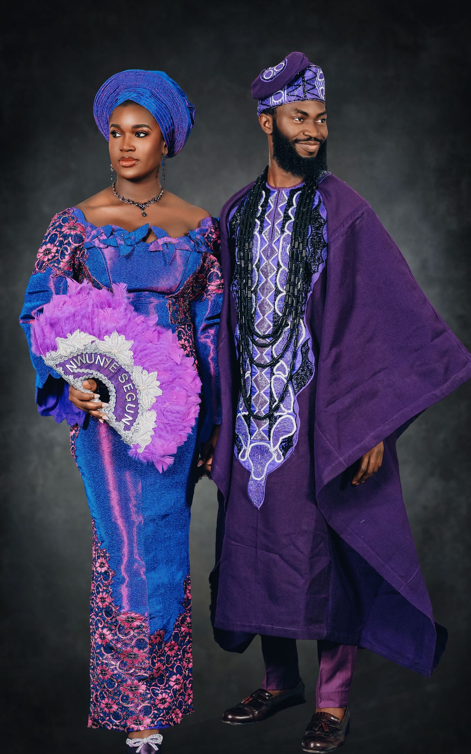 Couple wearing coordinated purple and blue traditional African formal wear with intricate embroidery designs.