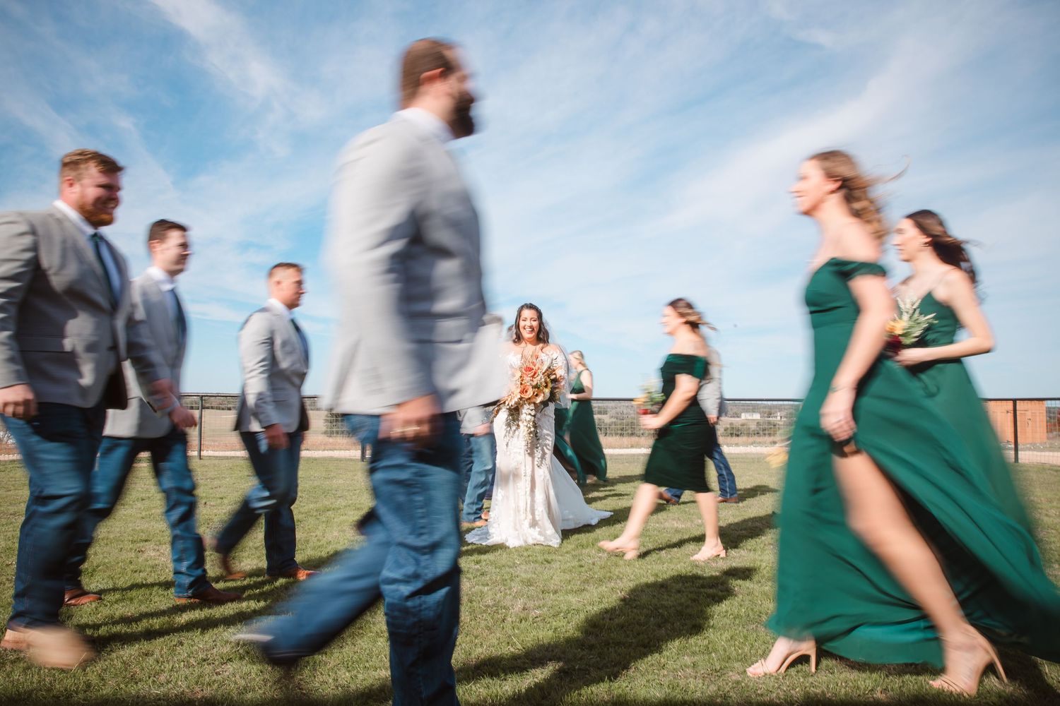 A creative motion blur photo of a wedding party walking across a field under blue skies.