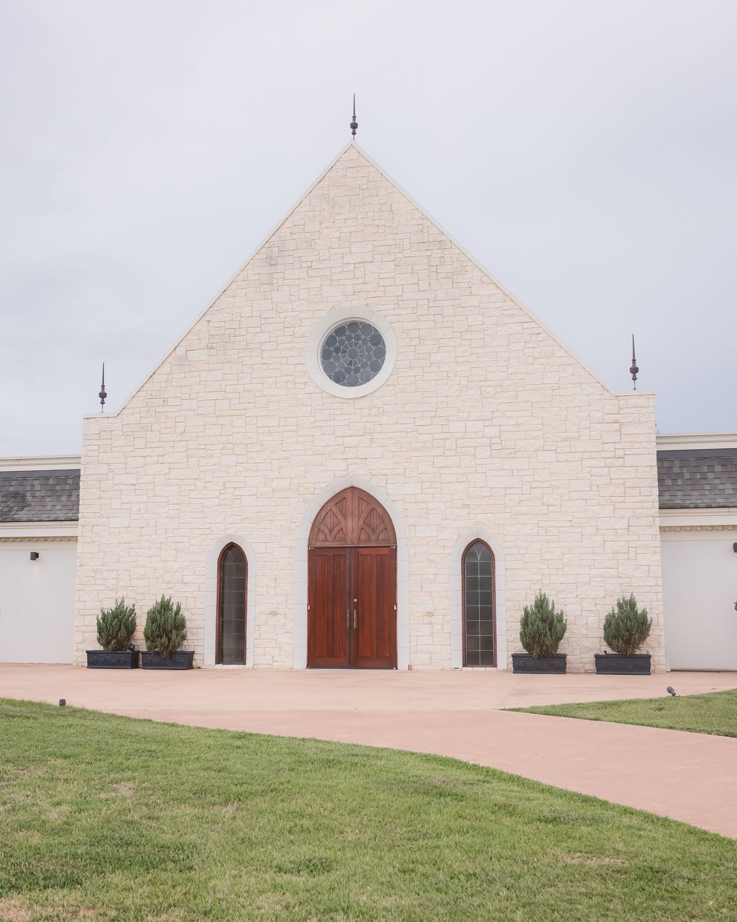 Modern white church exterior with clean architectural lines and wooden doors against a cloudy sky.