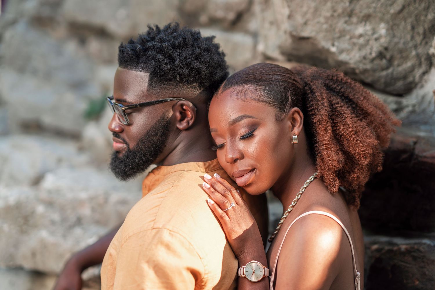 A couple embraces tenderly against a textured stone wall background.