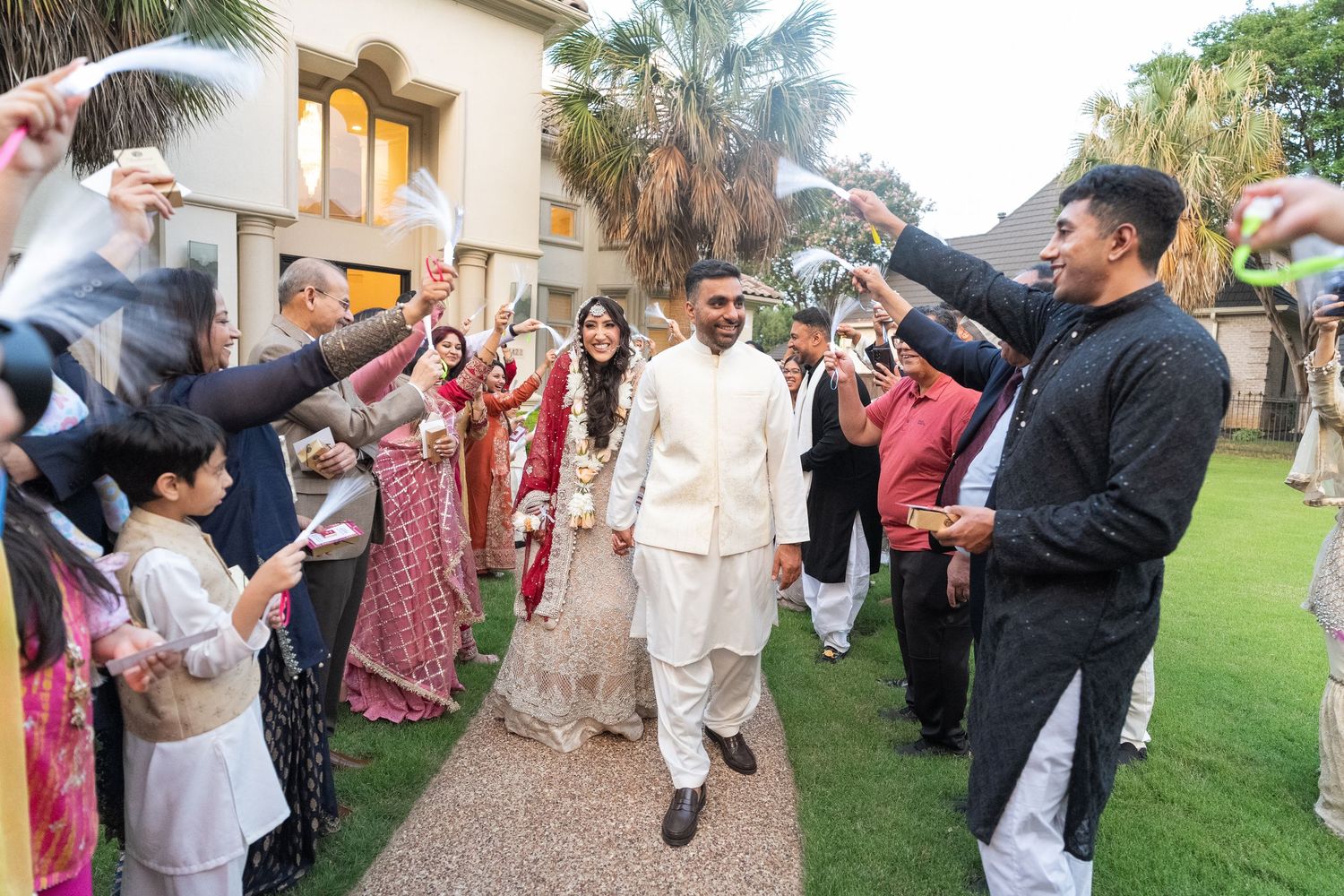 Wedding guests dancing and celebrating outdoors on a lawn during a festive reception party.