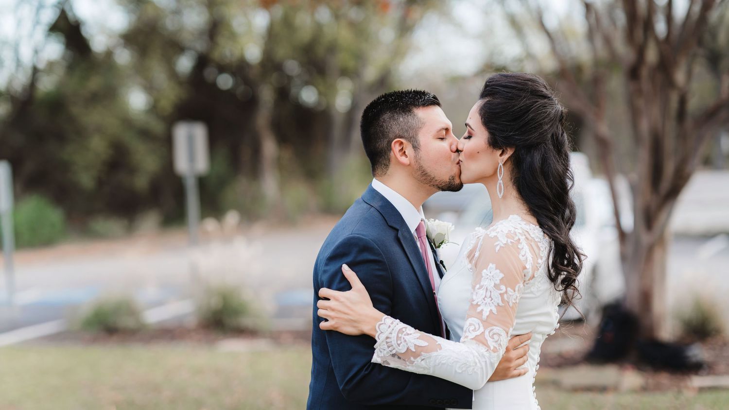 A romantic couple shares a tender kiss on a tree-lined path during an outdoor photo session.