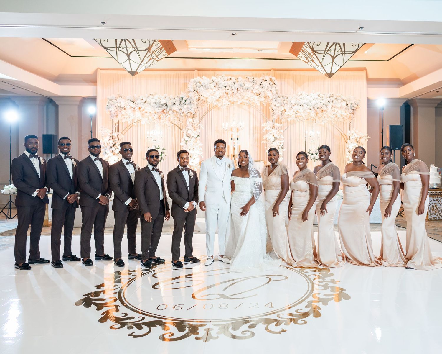 Elegant wedding party lineup in black and white attire posed in a grand ballroom with crystal chandeliers.