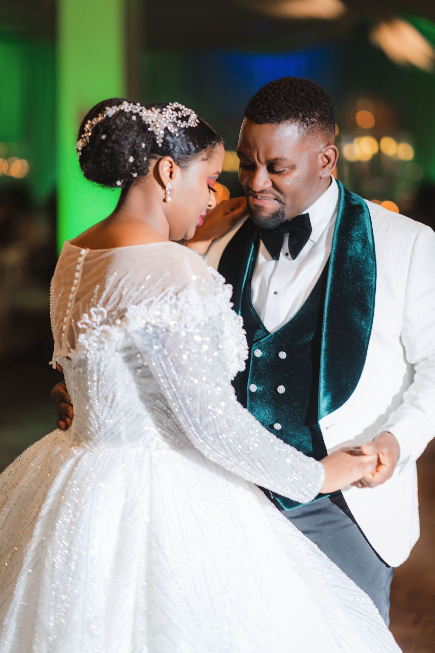 An intimate wedding moment captured under green and blue lighting with elegant formal attire.