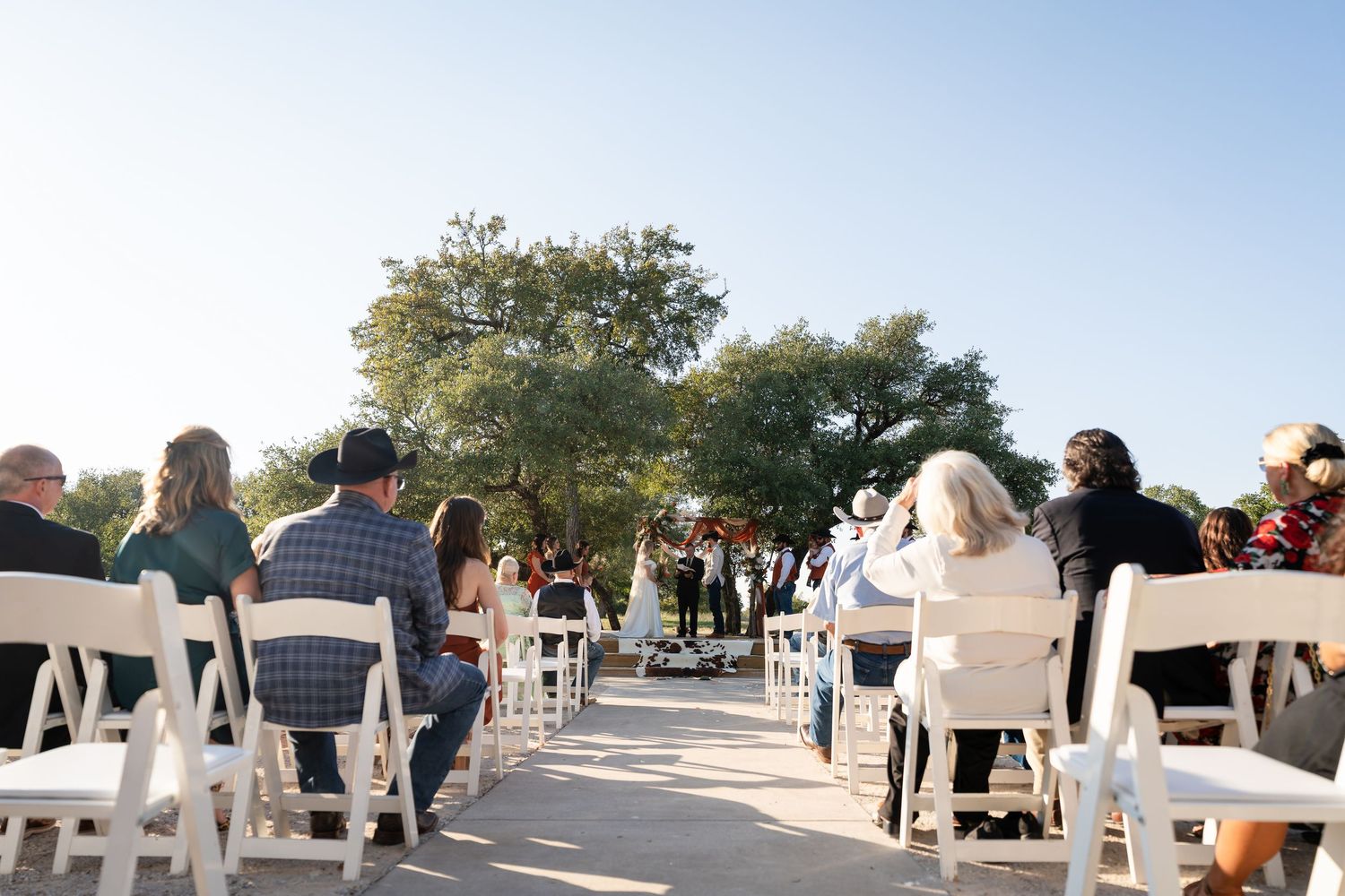 Panoramic view of an outdoor wedding reception setup with white chairs and rustic barn buildings.
