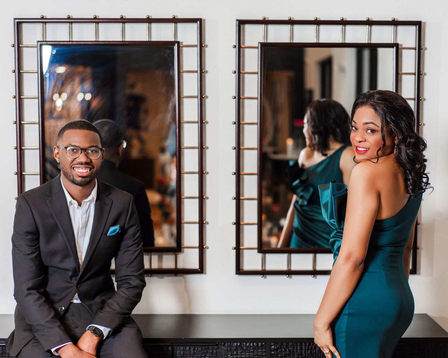Elegant couple in formal attire poses together during engagement photoshoot in a stylish indoor venue.
