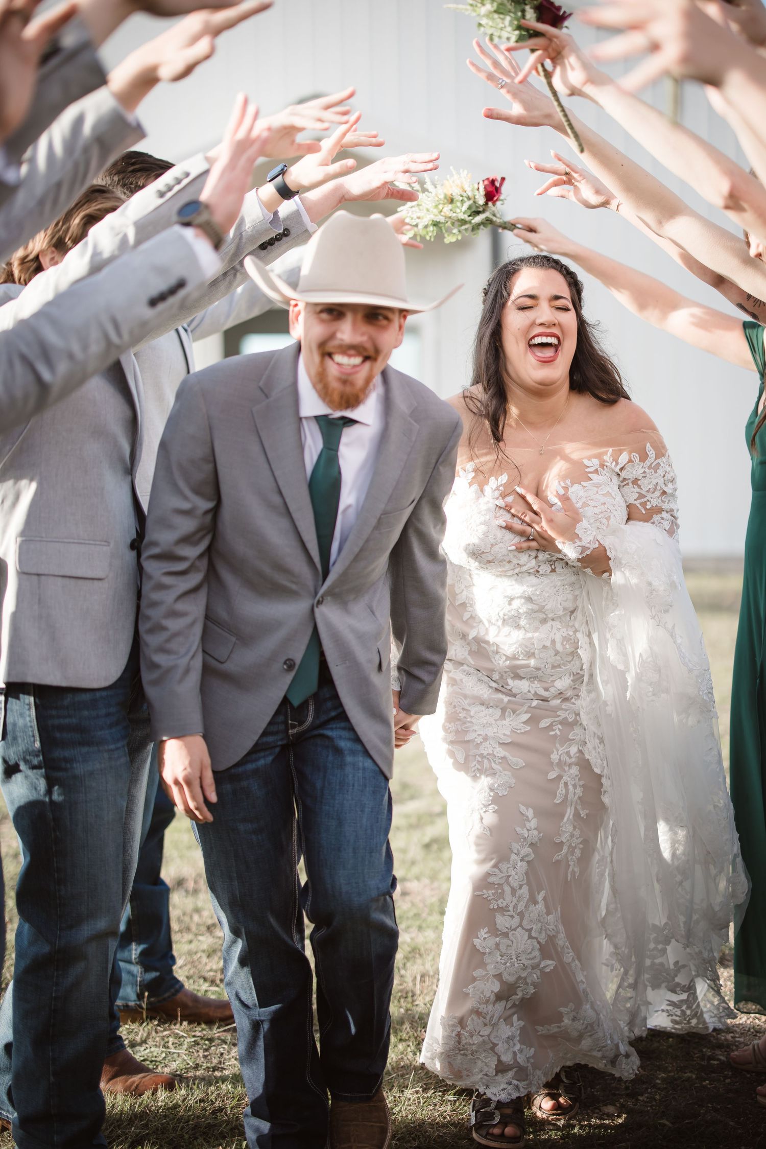 Wedding party members jump and celebrate joyfully on grassy grounds.