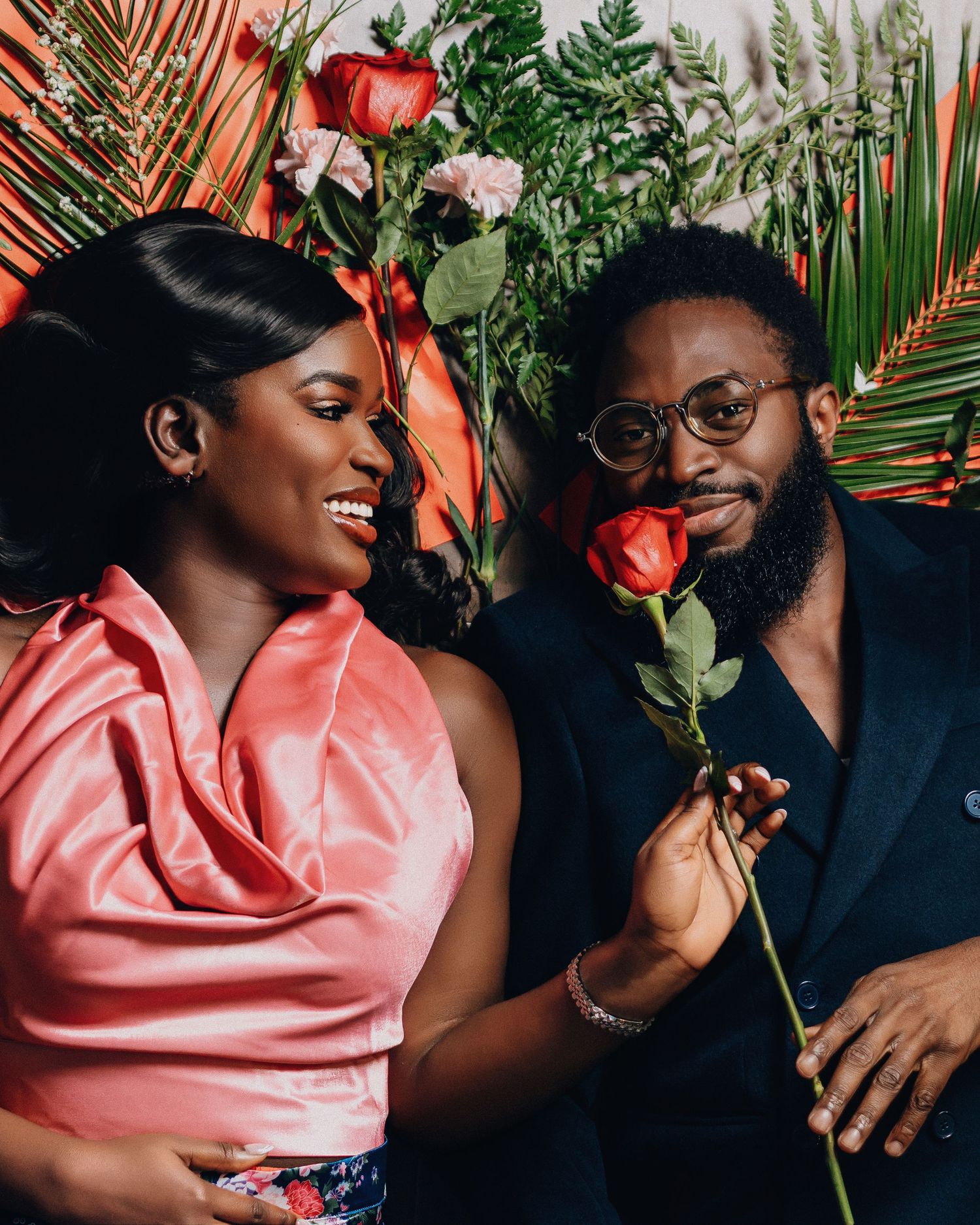 A romantic portrait with tropical leaves and red roses against coral and teal backdrop.
