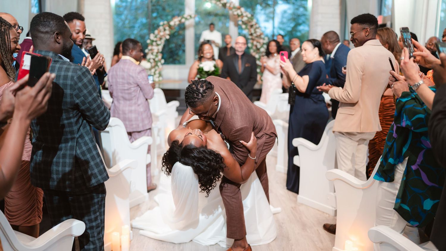 Wedding celebration scene showing a couple sharing a romantic dip-style dance move surrounded by applauding guests.