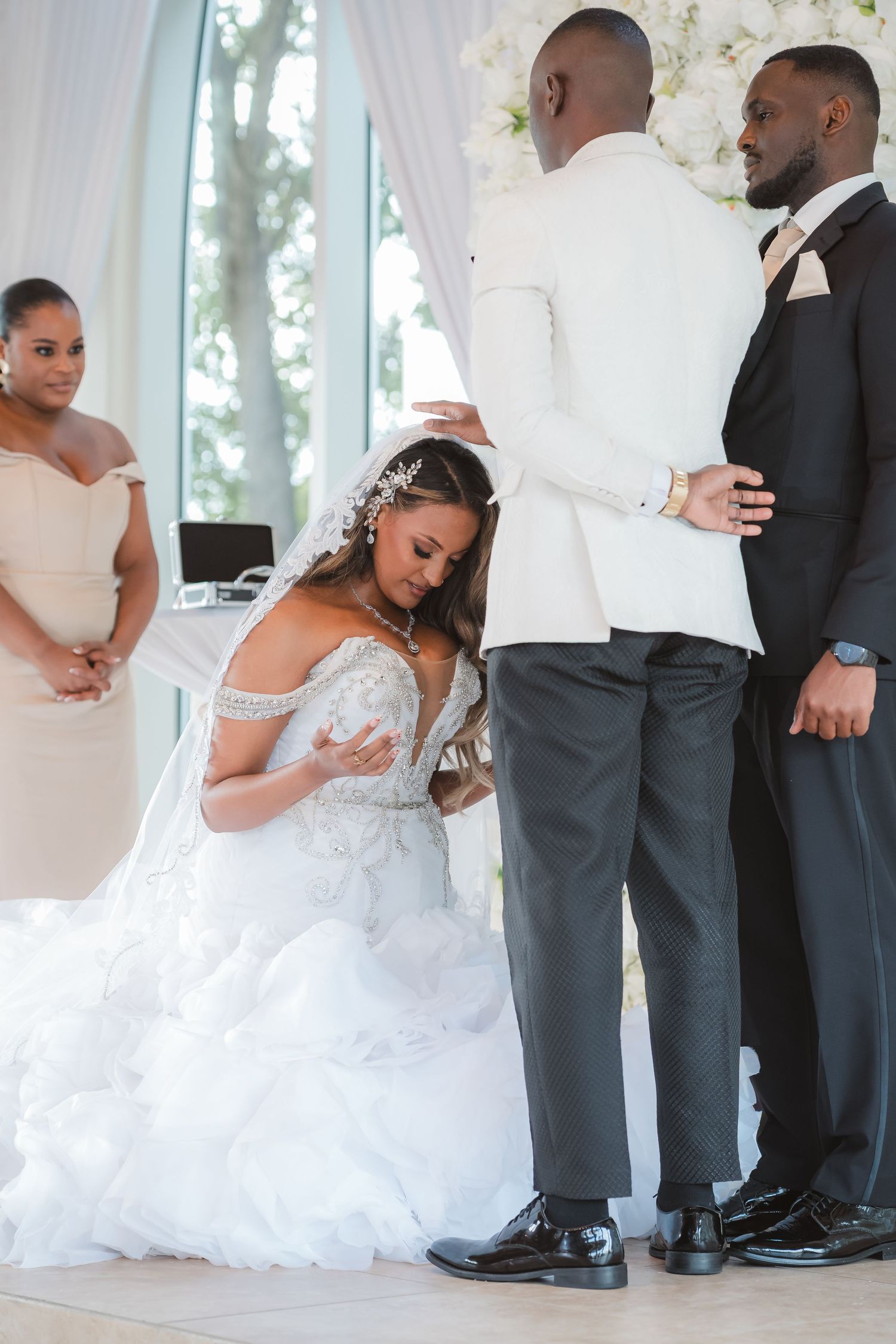 Wedding party members in formal attire gather during a celebration with flowing white dresses and dark suits.