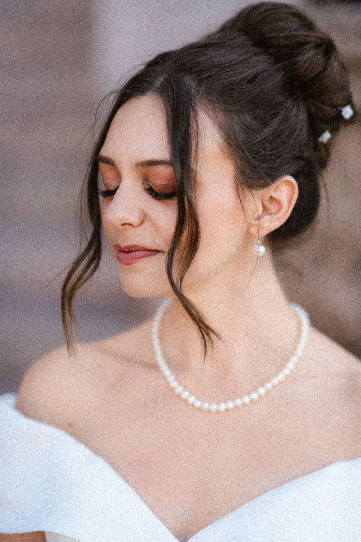 A pearl necklace adorns a bride's neck with elegant updo hairstyling.