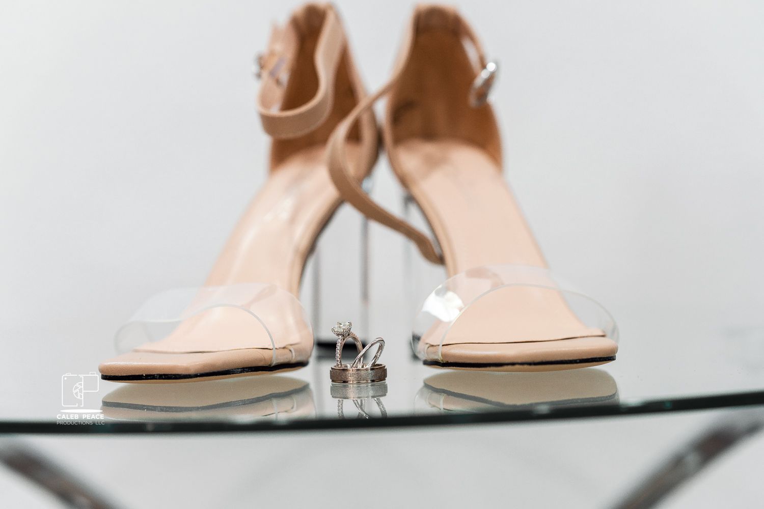 Nude wedding heels and rings displayed on glass surface in elegant bridal styling shot.