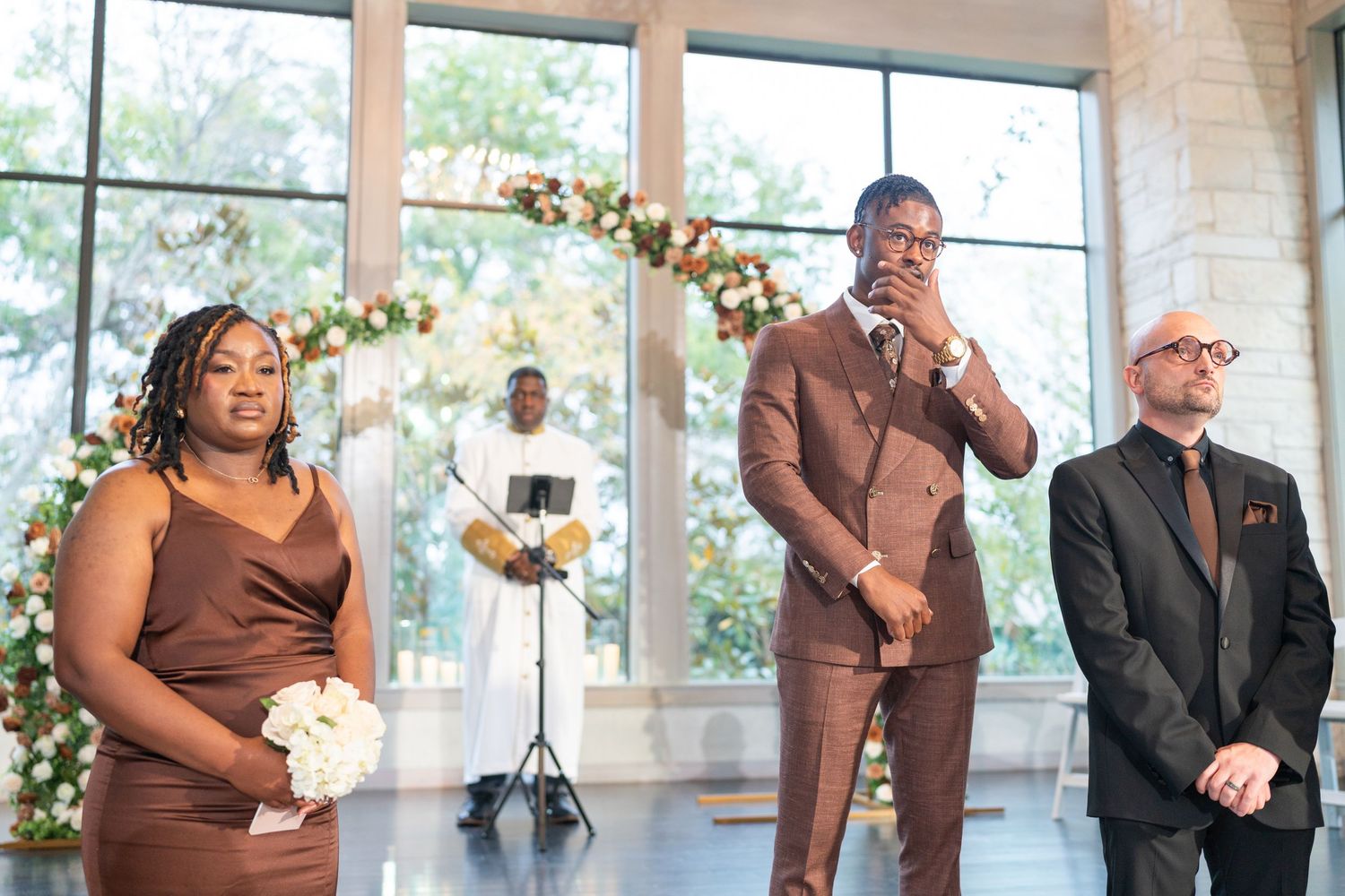 Wedding guests in formal attire mingling at an elegant venue with large windows.
