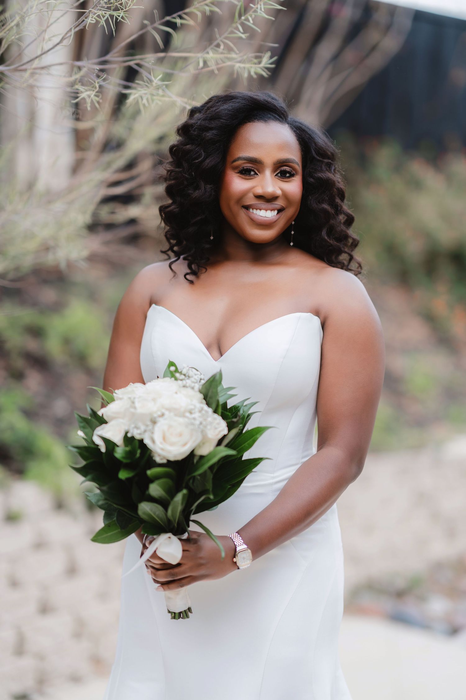 Beautiful bride in a white strapless wedding dress poses outdoors with a classic white floral bouquet.