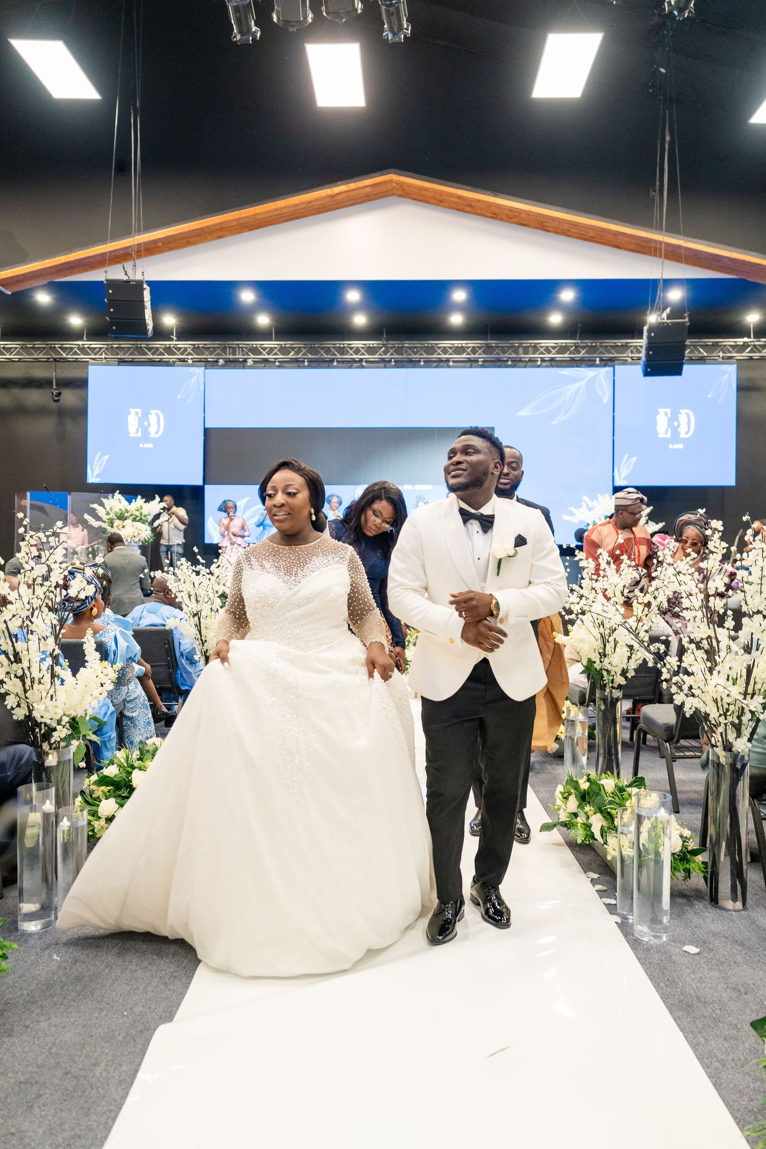 Wedding celebration in a modern venue with white floral arrangements and elegant lighting setup.
