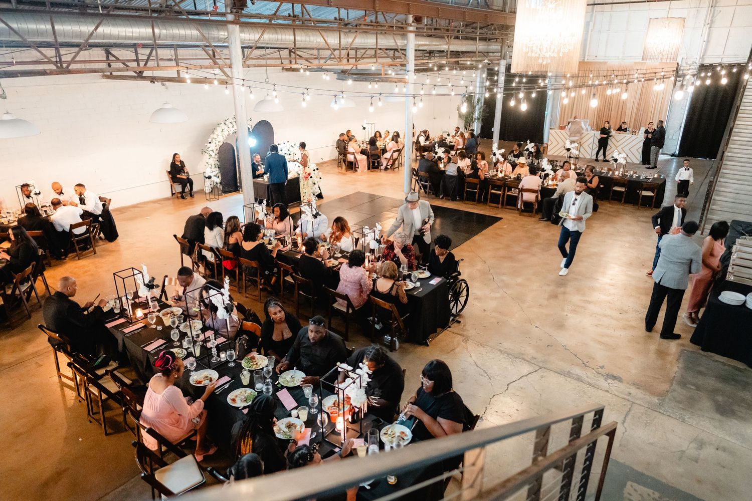 Wide panoramic view of wedding reception with guests seated at multiple tables.