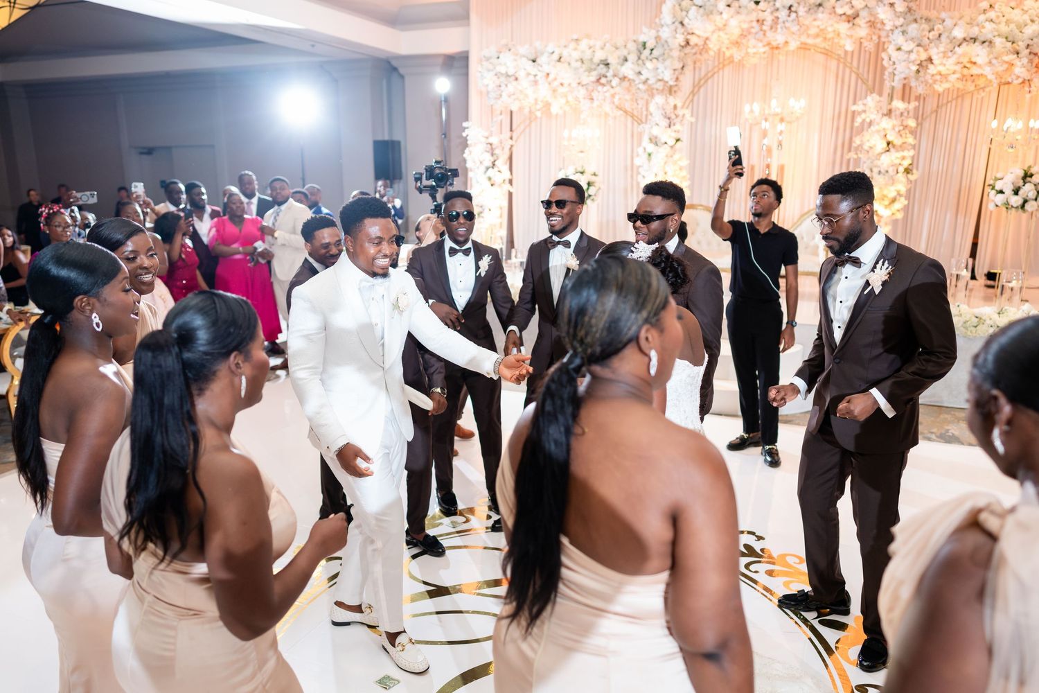 Wedding reception celebration with bridal party and guests dancing in an elegantly decorated ballroom.