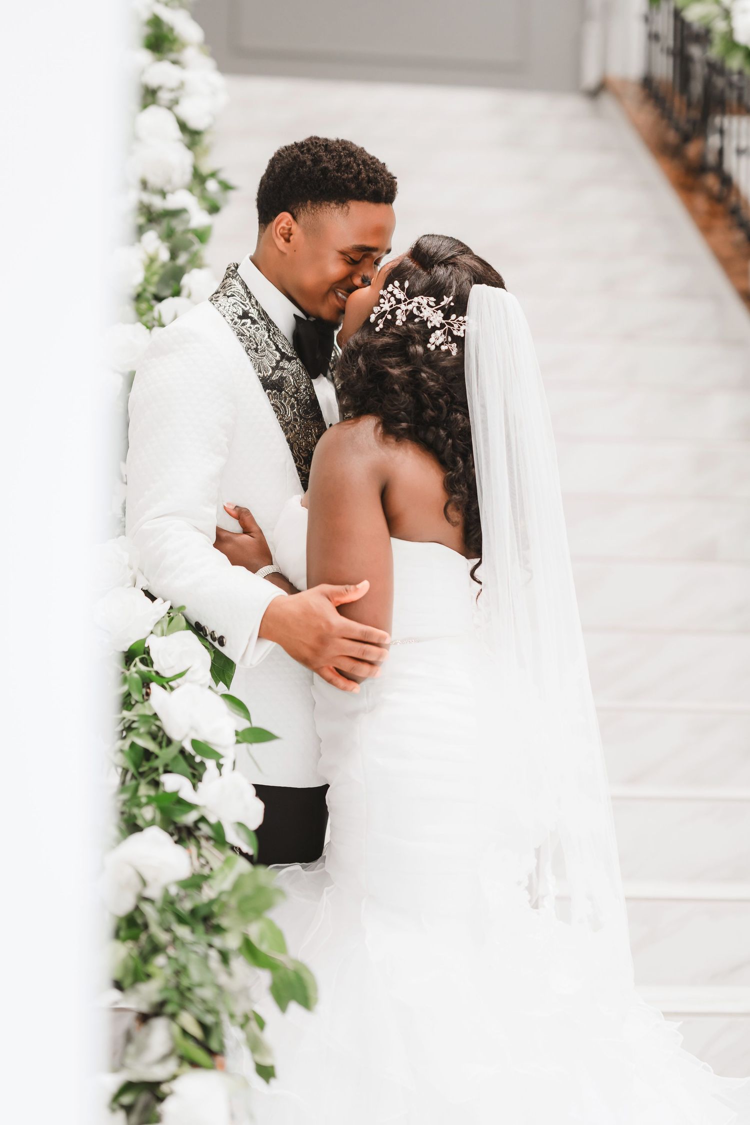 Elegant wedding couple embracing in front of a white floral arch during their ceremony.