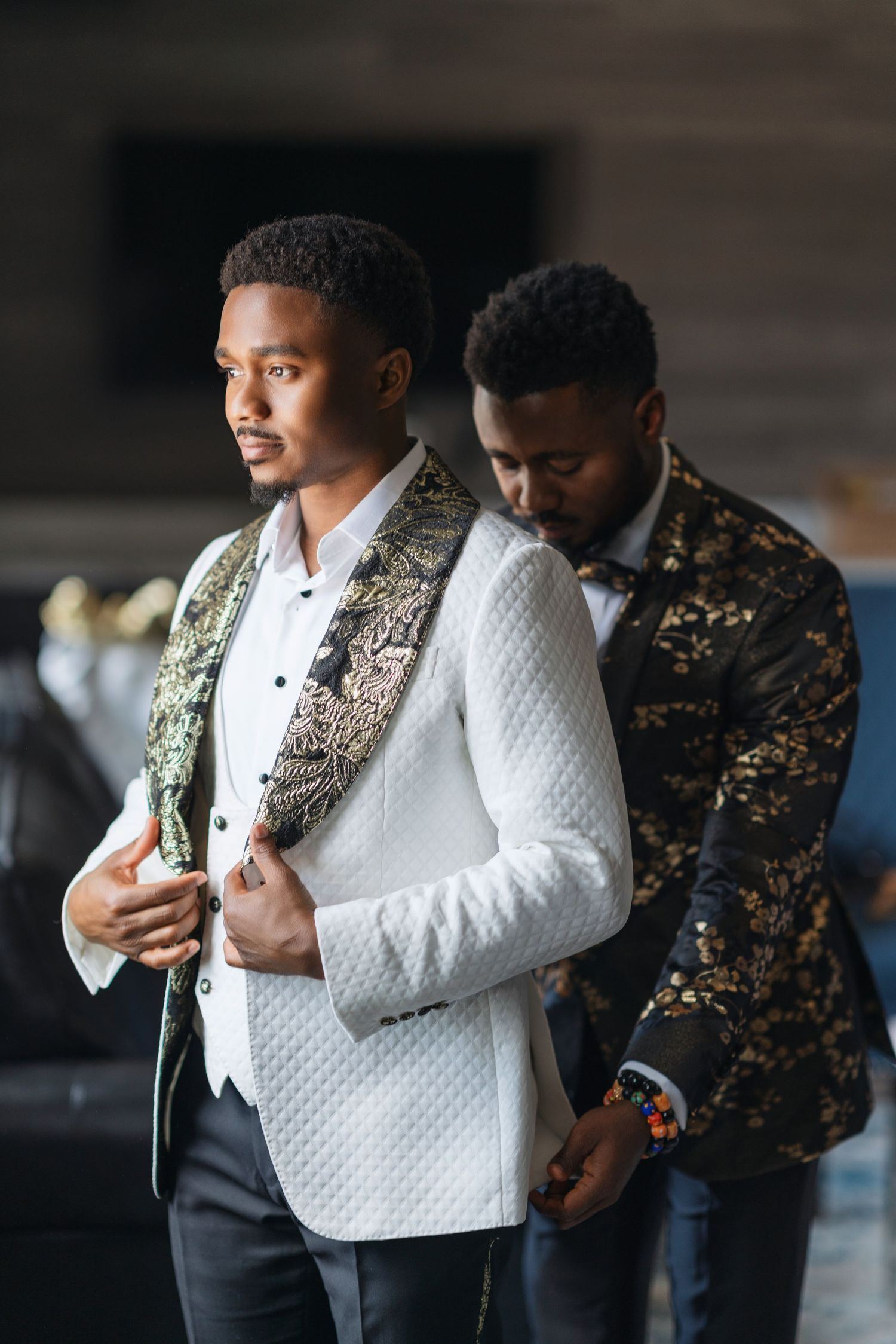 Formal attire being adjusted, featuring a white textured jacket with ornate gold trim details.