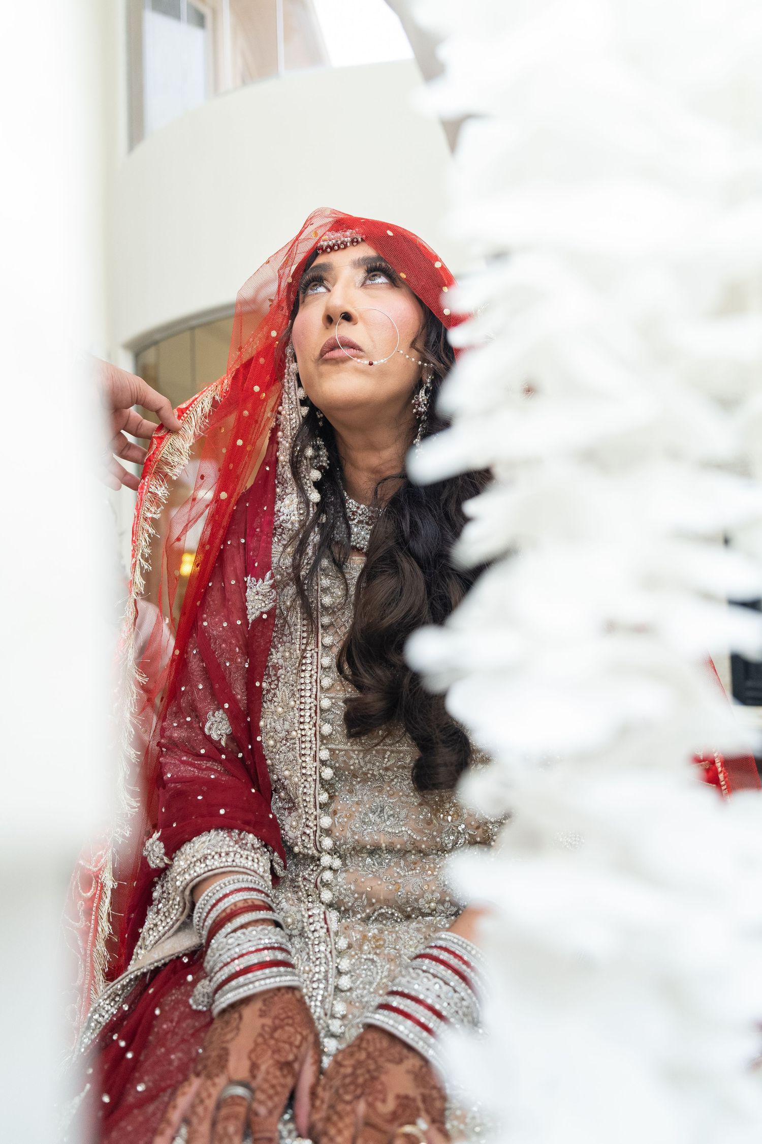 Artistic bridal portrait featuring traditional South Asian wedding attire with red dupatta and silver embellishments.