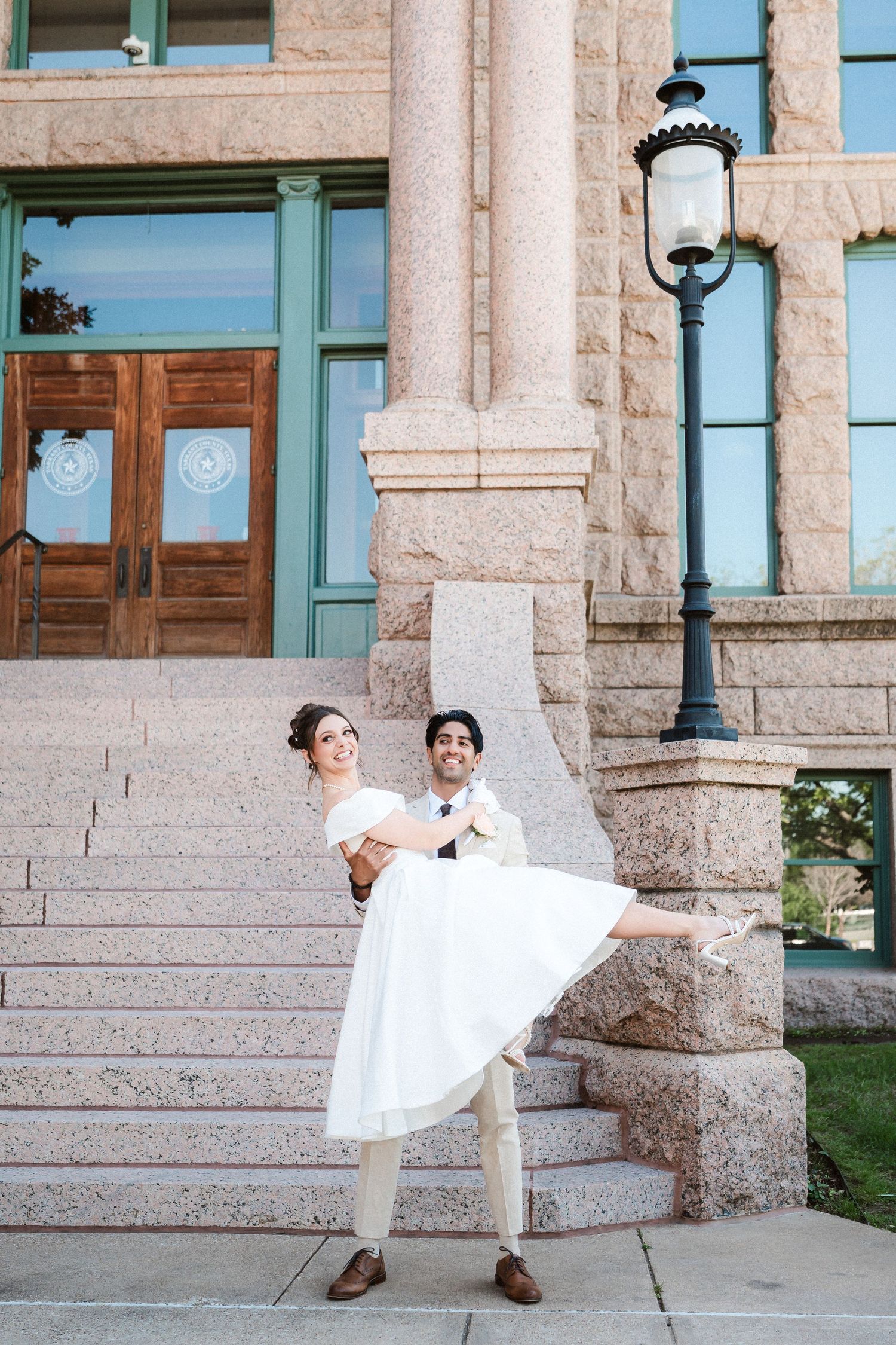 A wedding couple dancing and twirling on stone steps of a historic building with turquoise trim.