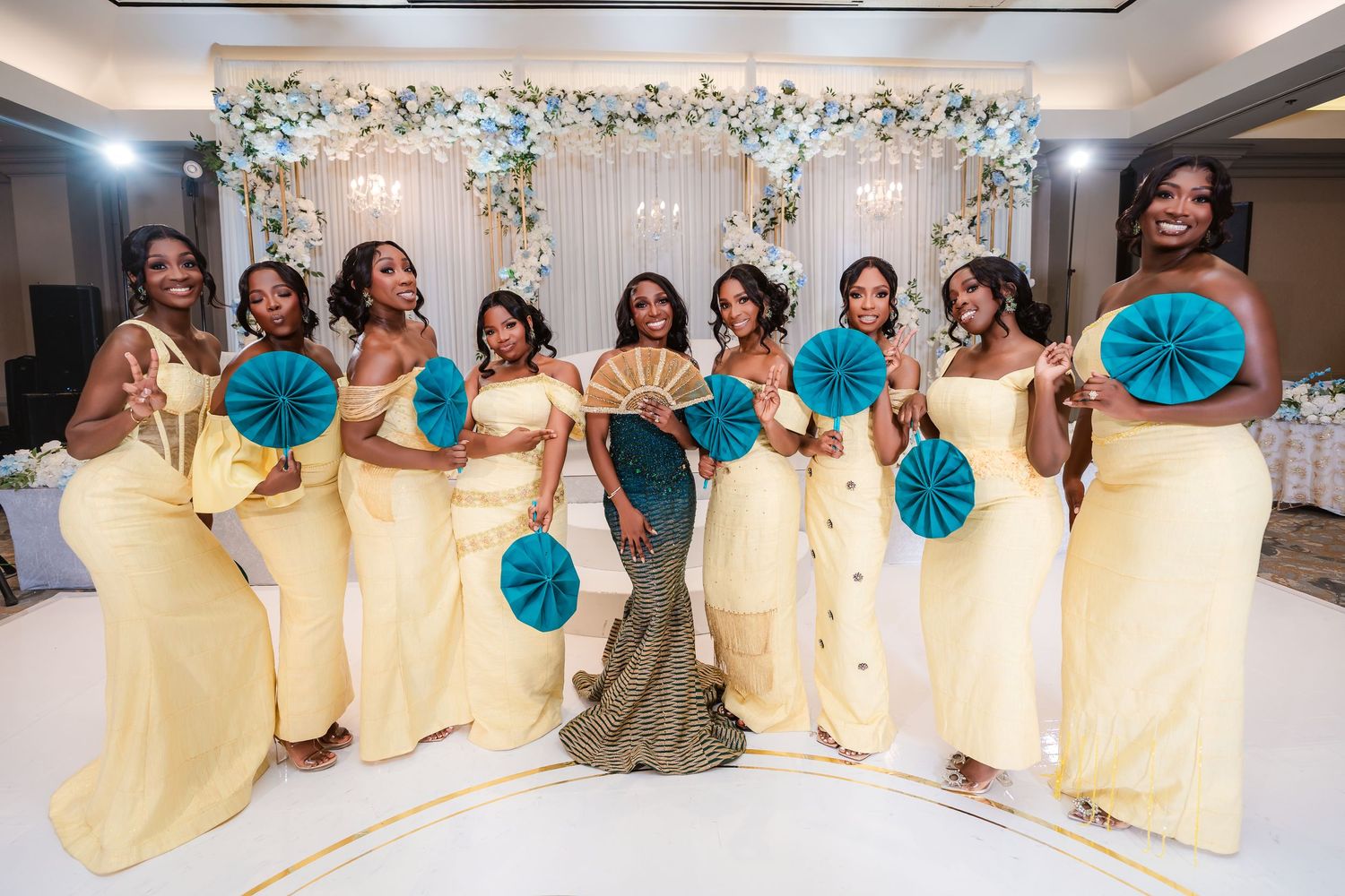Wedding party members in yellow dresses pose together at an elegant venue with floral decorations.