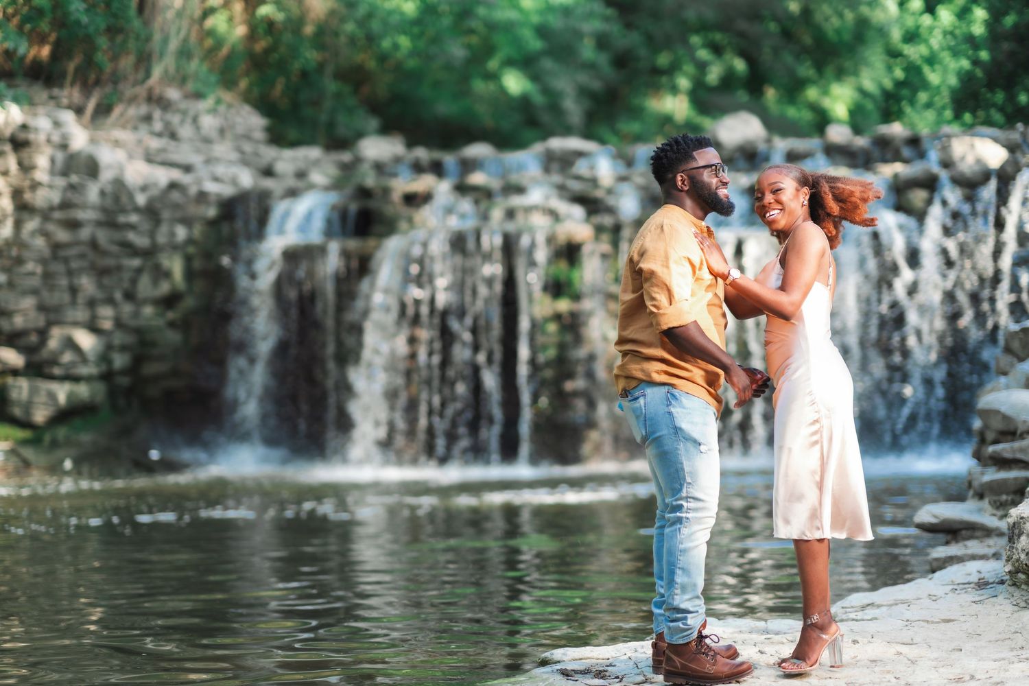 A couple shares intimate moments near a cascading waterfall in a romantic outdoor photoshoot.