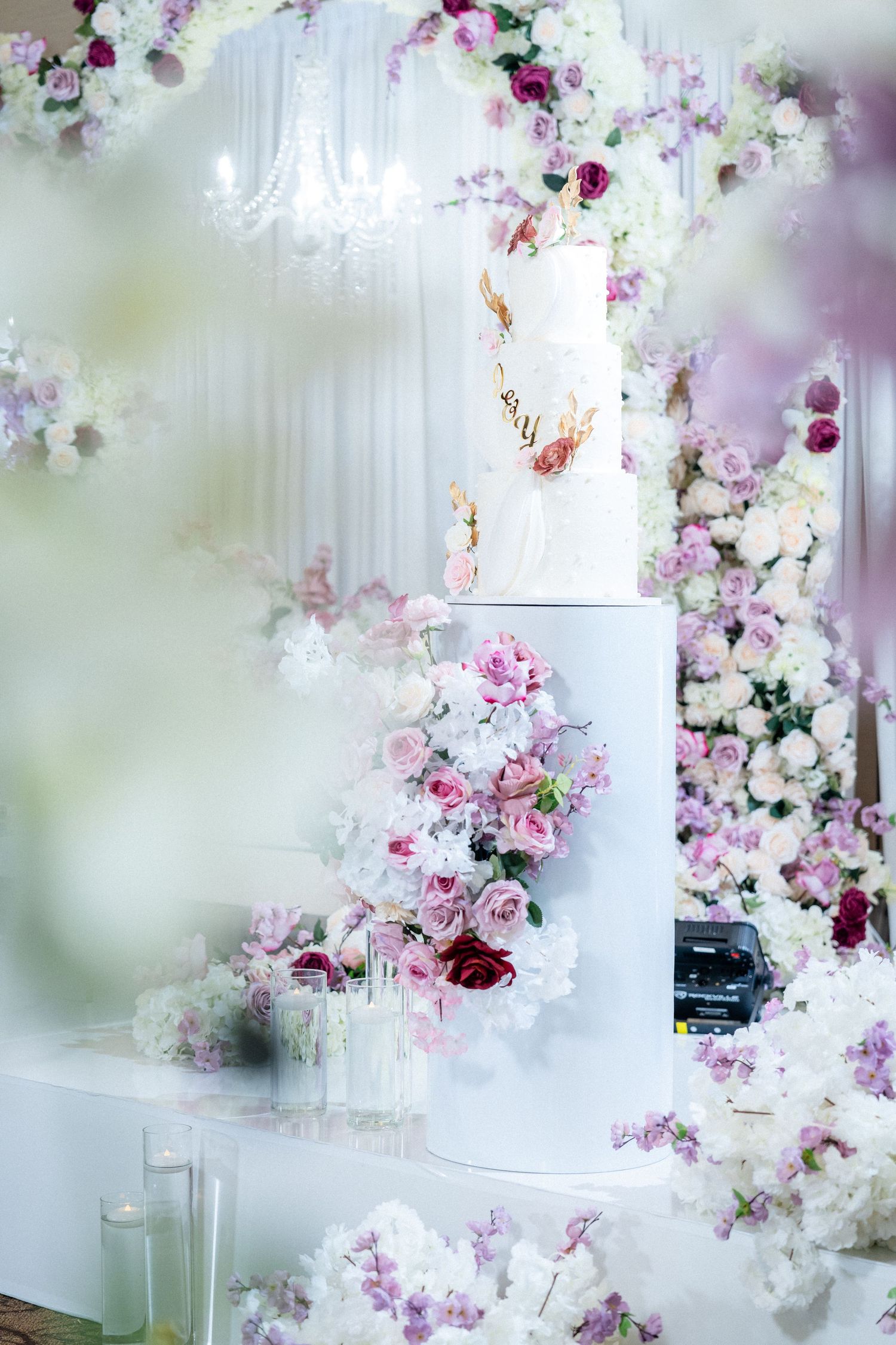An elegant white wedding cake decorated with pink and purple flowers against a floral backdrop.