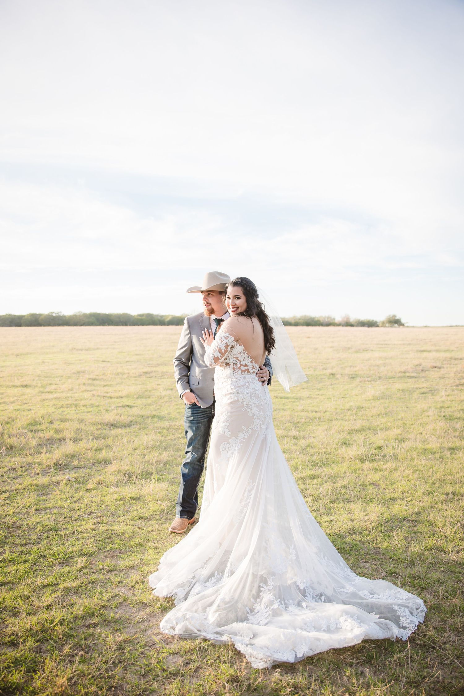 Romantic wedding couple embraces in a sun-drenched field with flowing white dress and golden light.