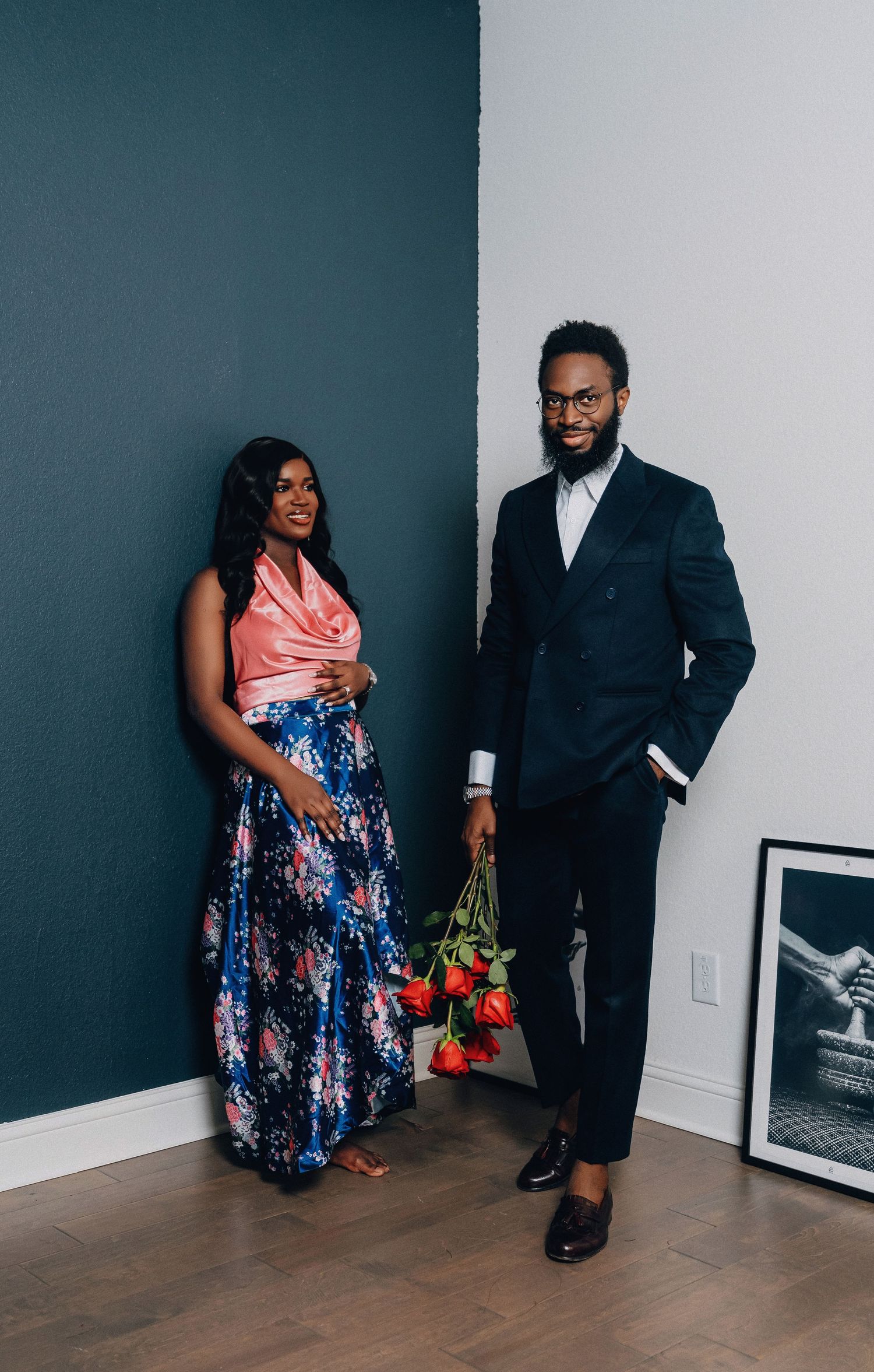 A couple poses playfully in formal attire, with the woman wearing a floral dress and the man in a dark suit.