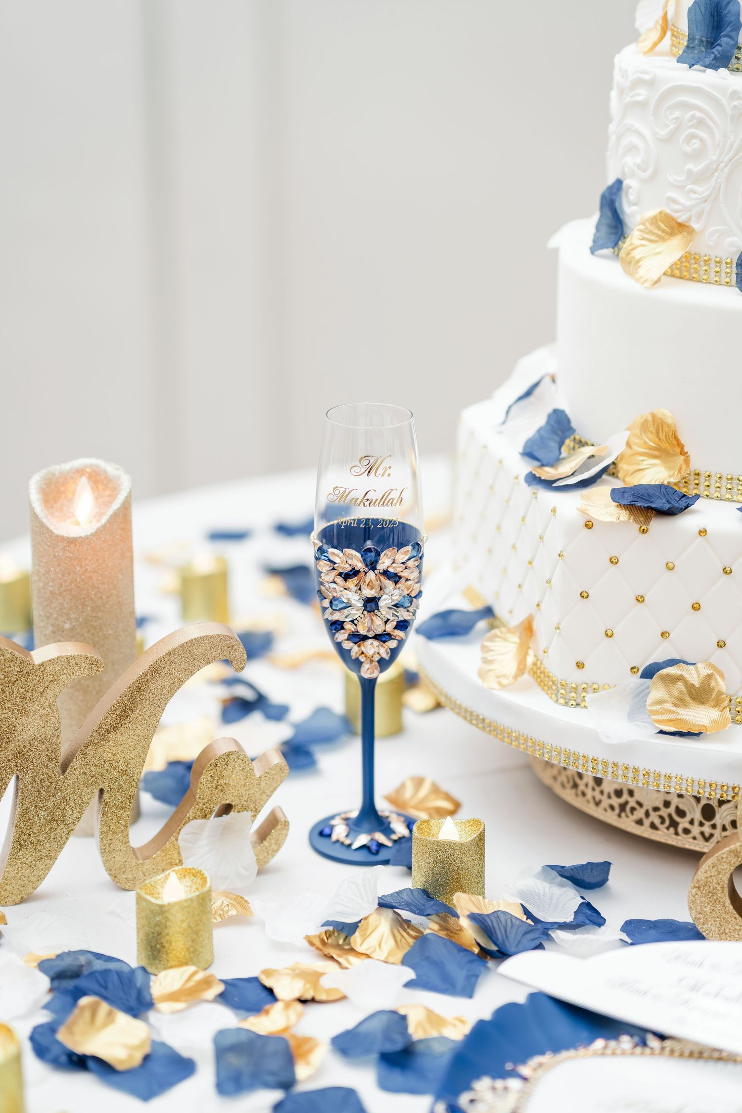Elegant wedding cake table decorated with blue and gold accents and scattered petals.