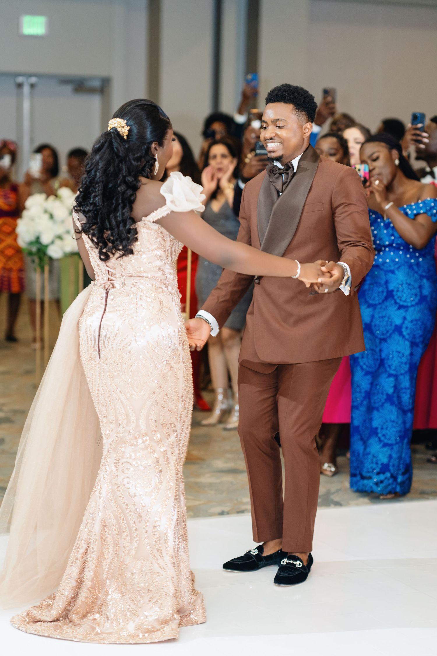 A couple dances together at a wedding reception, with the woman wearing a blush sequin gown.
