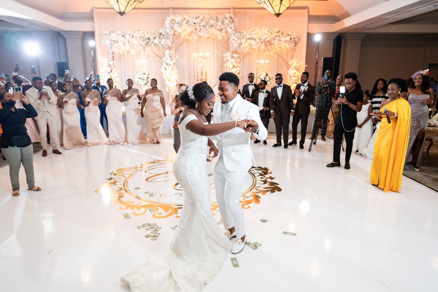 Romantic first dance moment at wedding reception with elegant floral backdrop and white dance floor.
