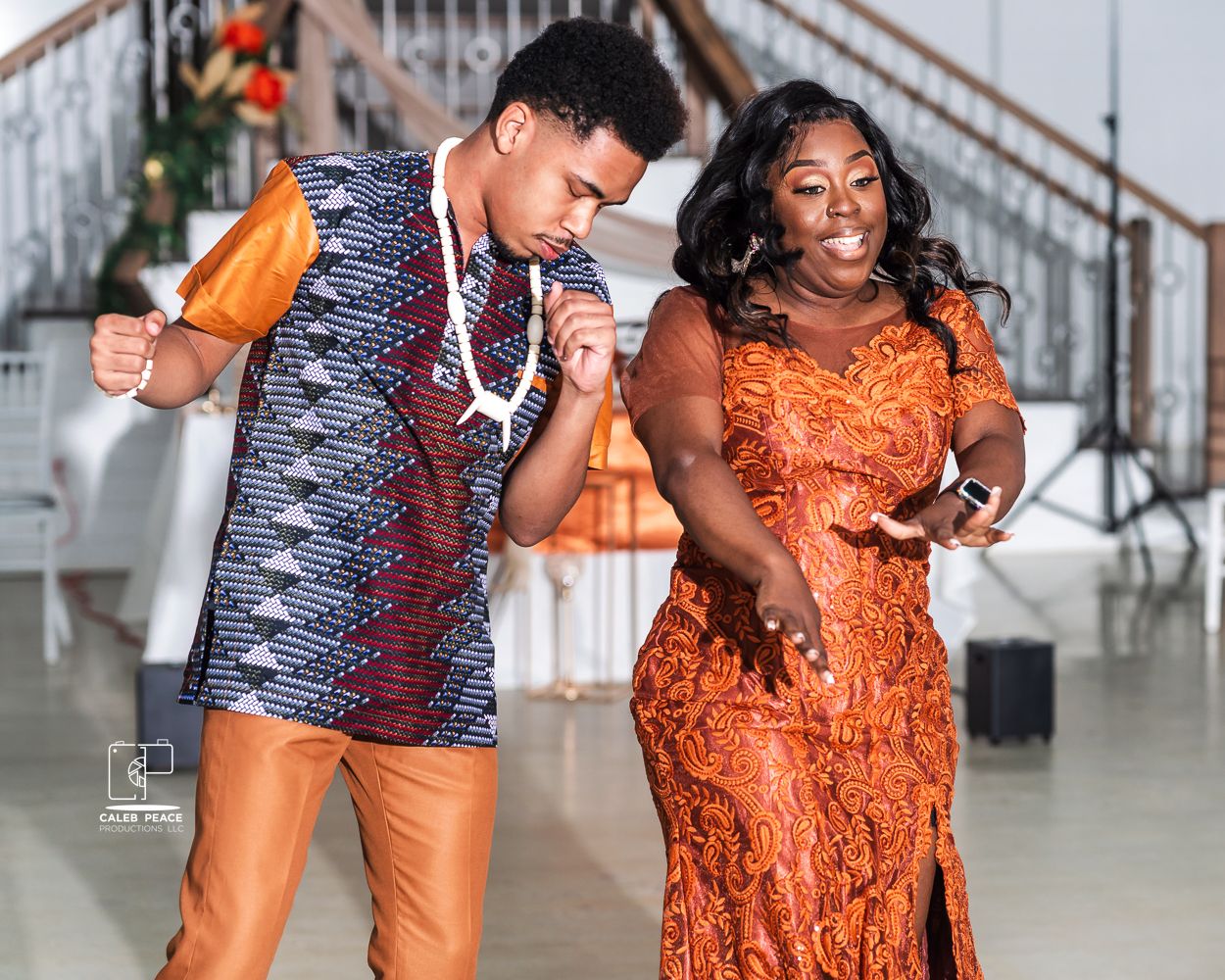 Wedding party members dance and celebrate in vibrant orange and blue outfits.
