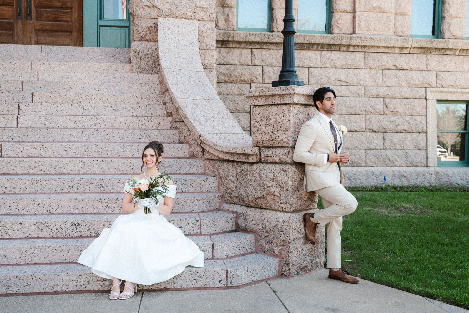 A couple in wedding attire poses separately on stone steps outside a historic building.