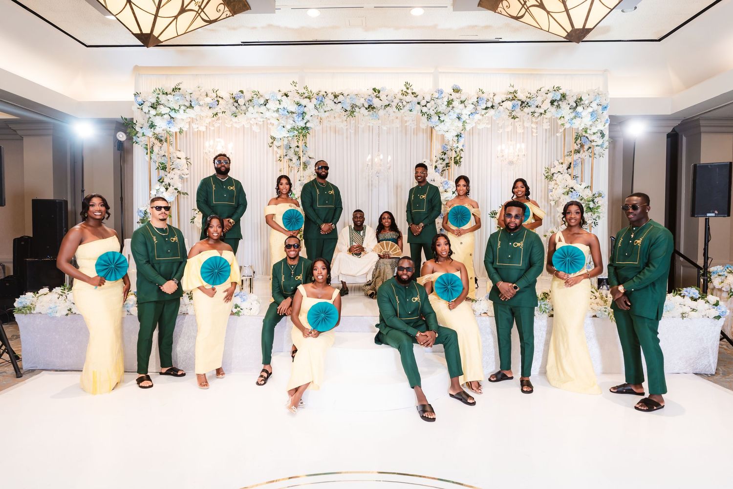 Wedding party lineup in coordinated emerald green and cream formal attire against a floral backdrop.