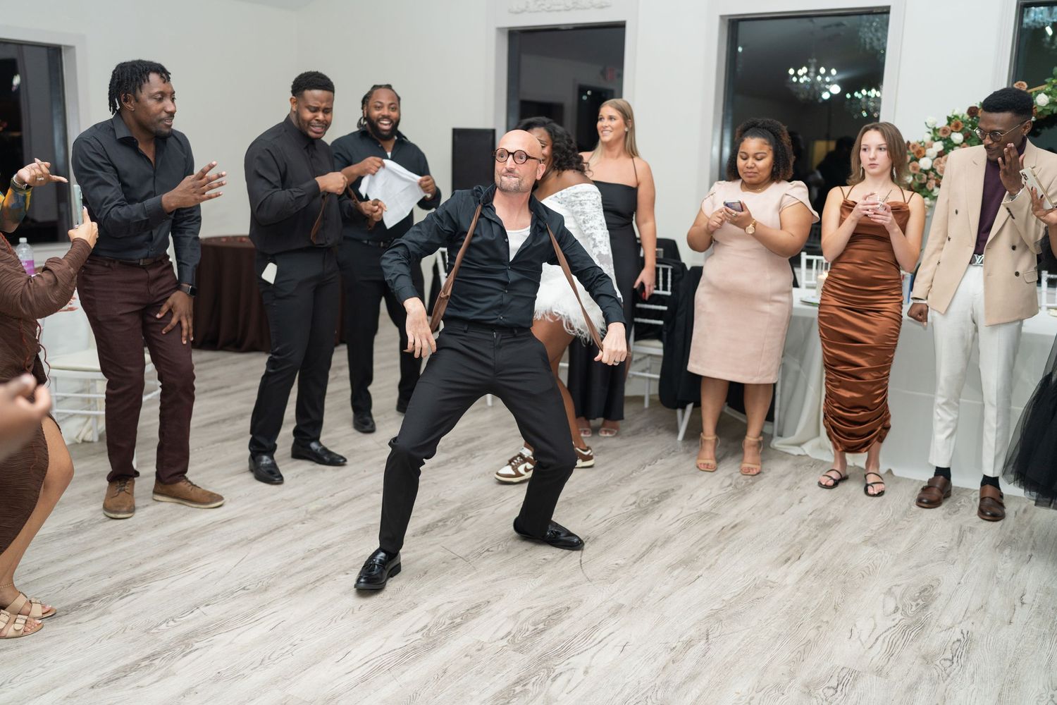Wedding reception guests dancing and celebrating in a white-walled venue.