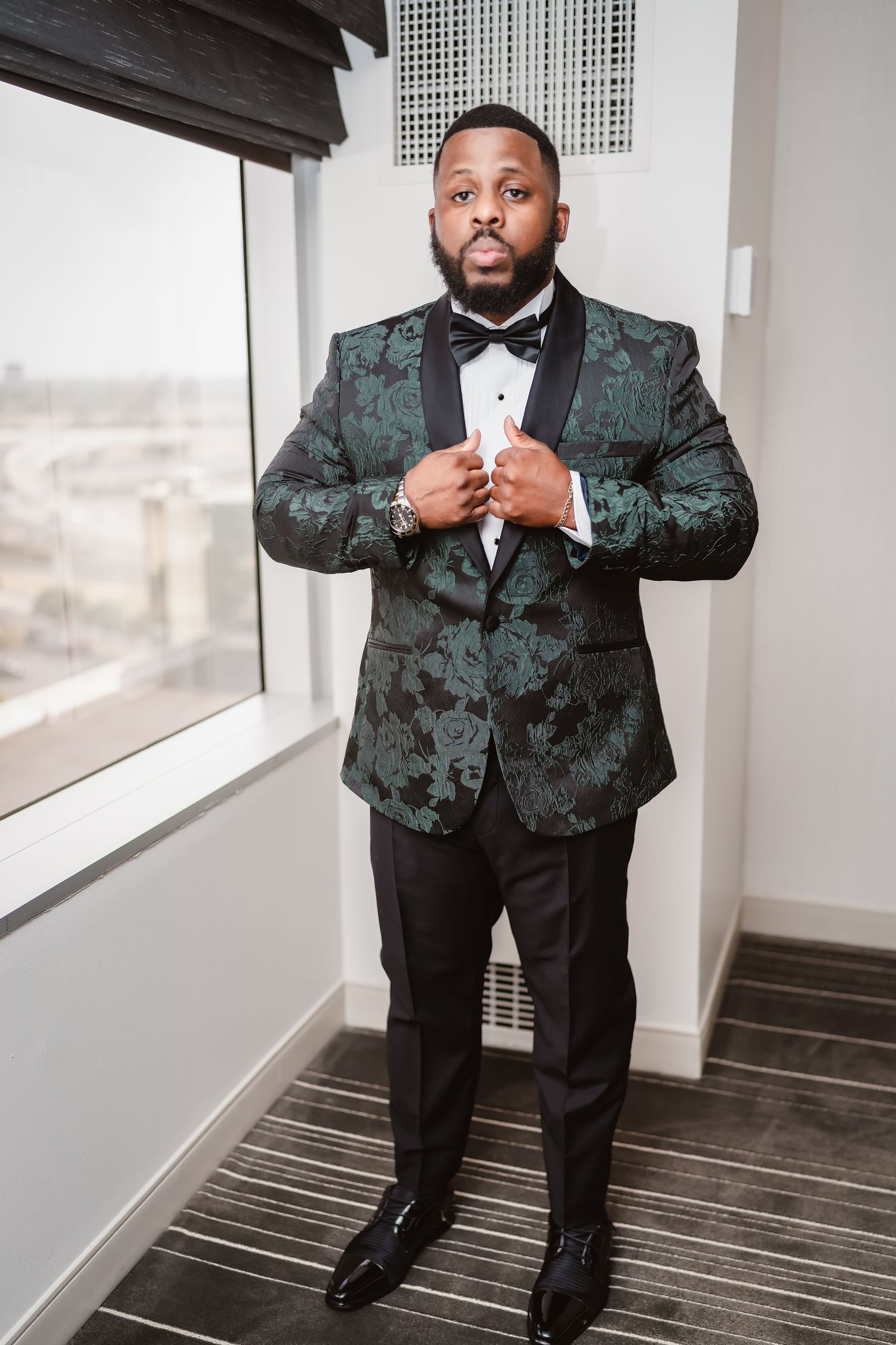 Groom in a patterned dark green tuxedo jacket poses confidently in an elegant indoor setting.