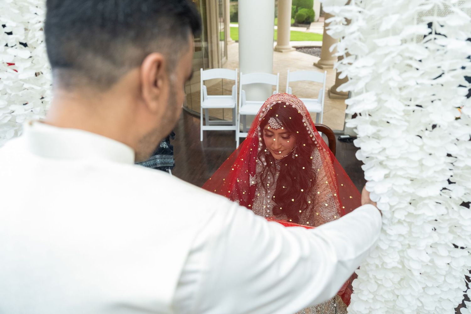 Wedding couple poses under hanging crystal decorations and floral arrangements.