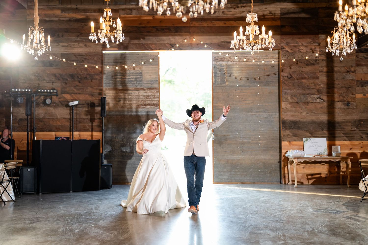 Rustic barn wedding venue interior with crystal chandeliers and wooden beams.