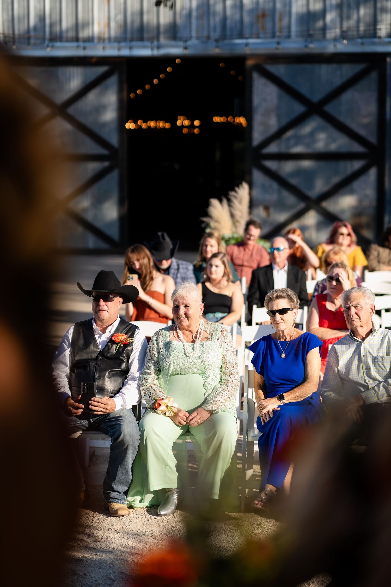 Wedding guests seated outdoors watching a ceremony at sunset with string lights overhead.