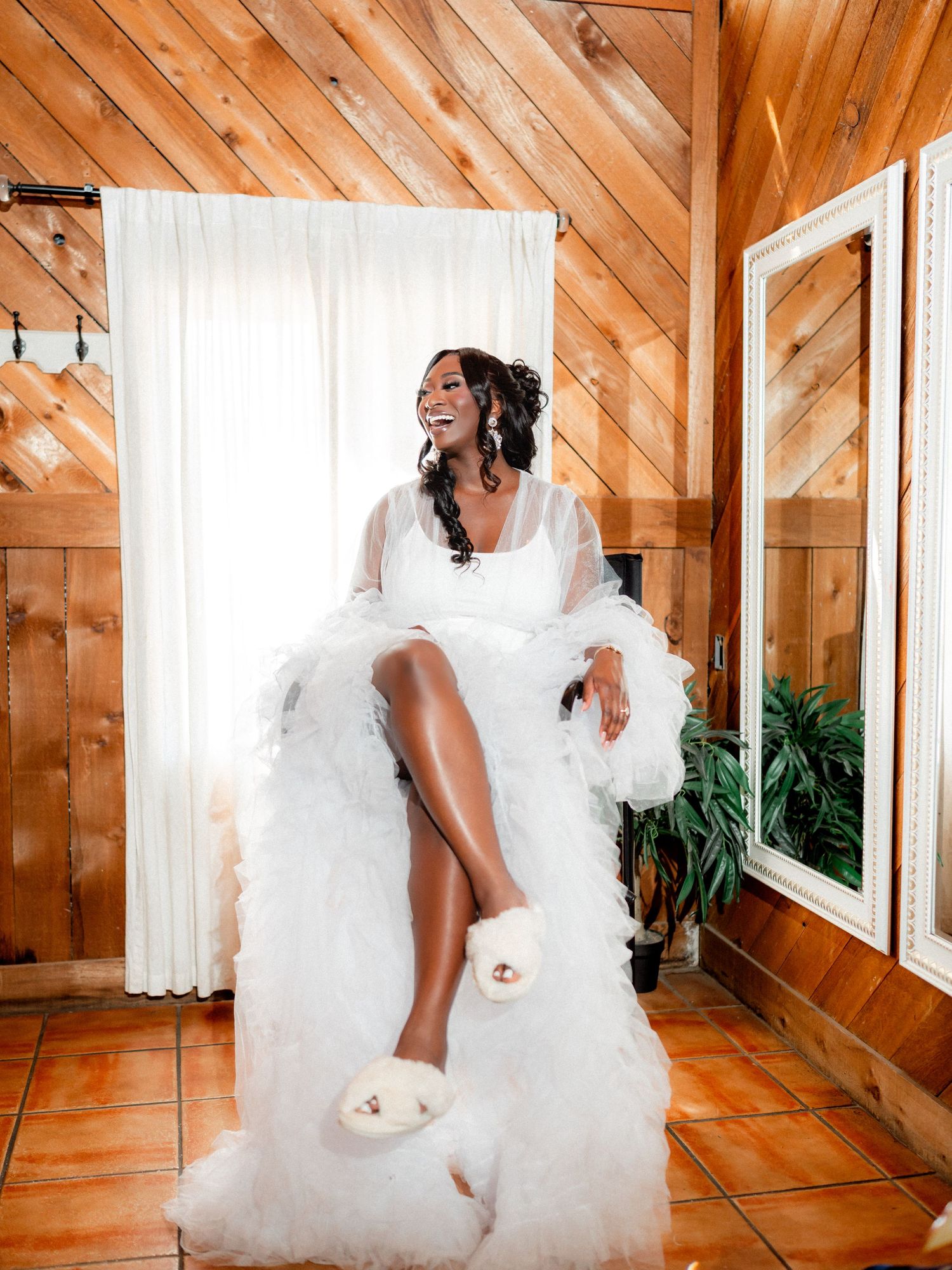 A wedding dress hangs in a rustic wooden room with natural lighting and hardwood floors.