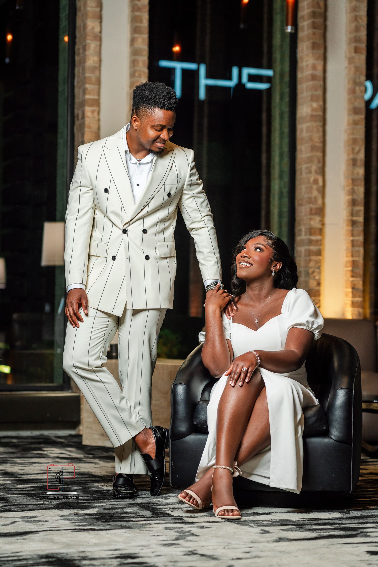 A stylish fashion photoshoot featuring a white pinstripe suit and white dress against an urban backdrop.