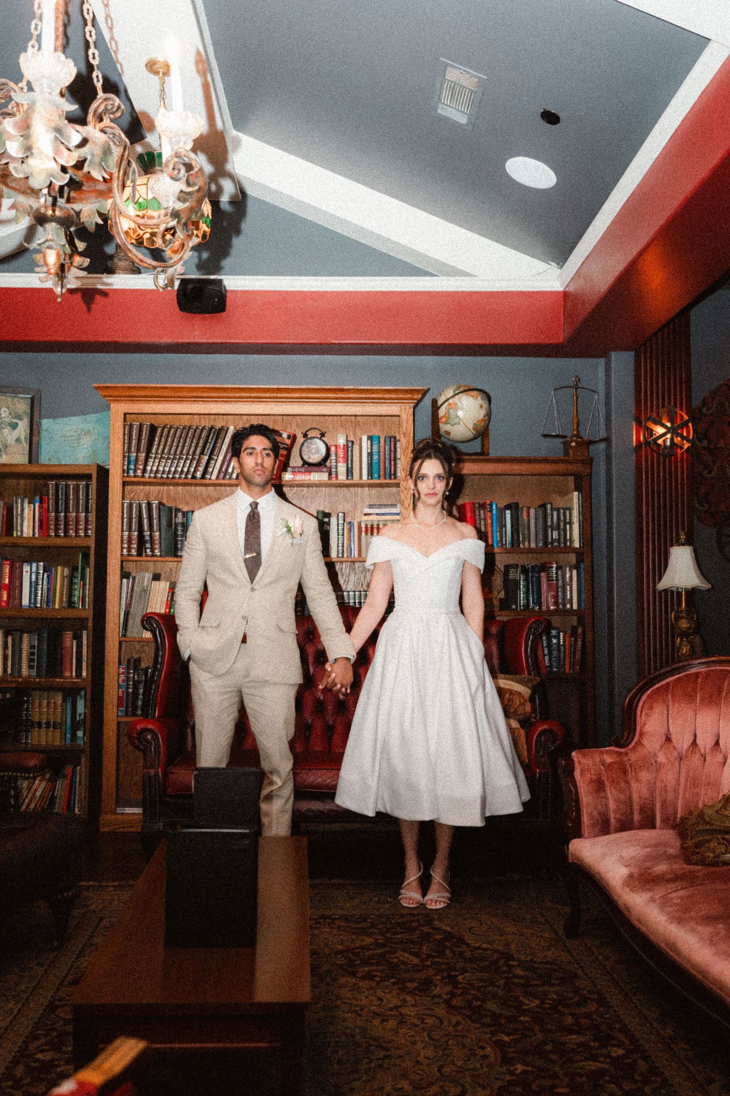 A couple dances together in a library room with bookshelves and red couches.