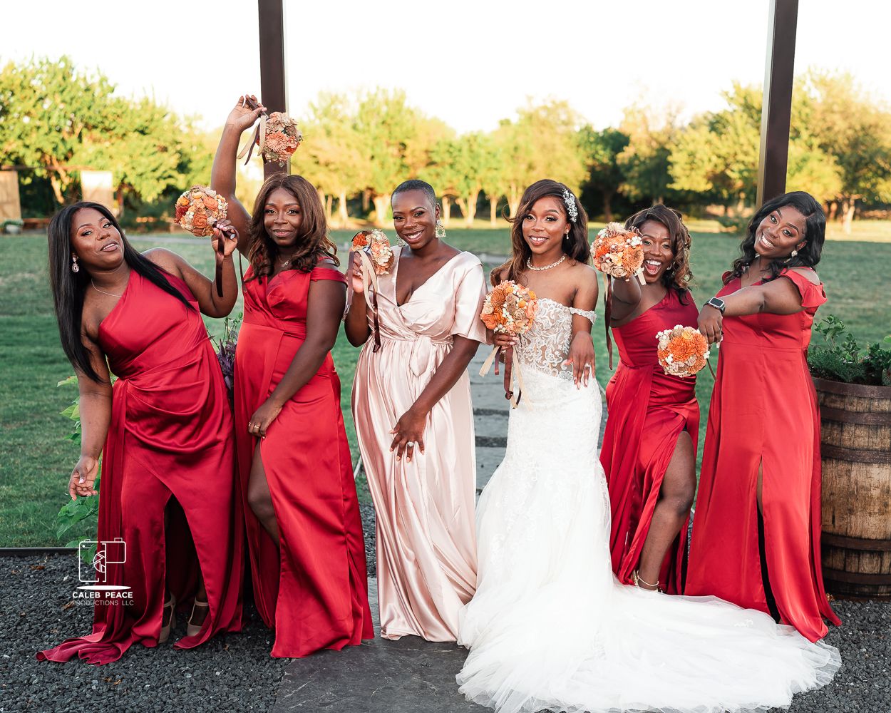 Wedding party in red dresses and white gown celebrating outdoors at sunset.