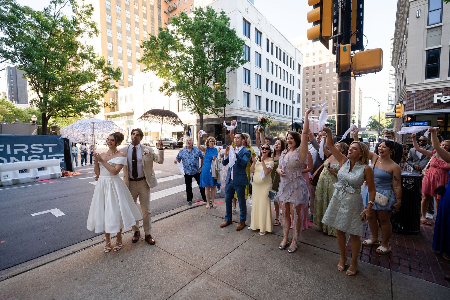 Wedding party processional walking down urban sidewalk with buildings in background.
