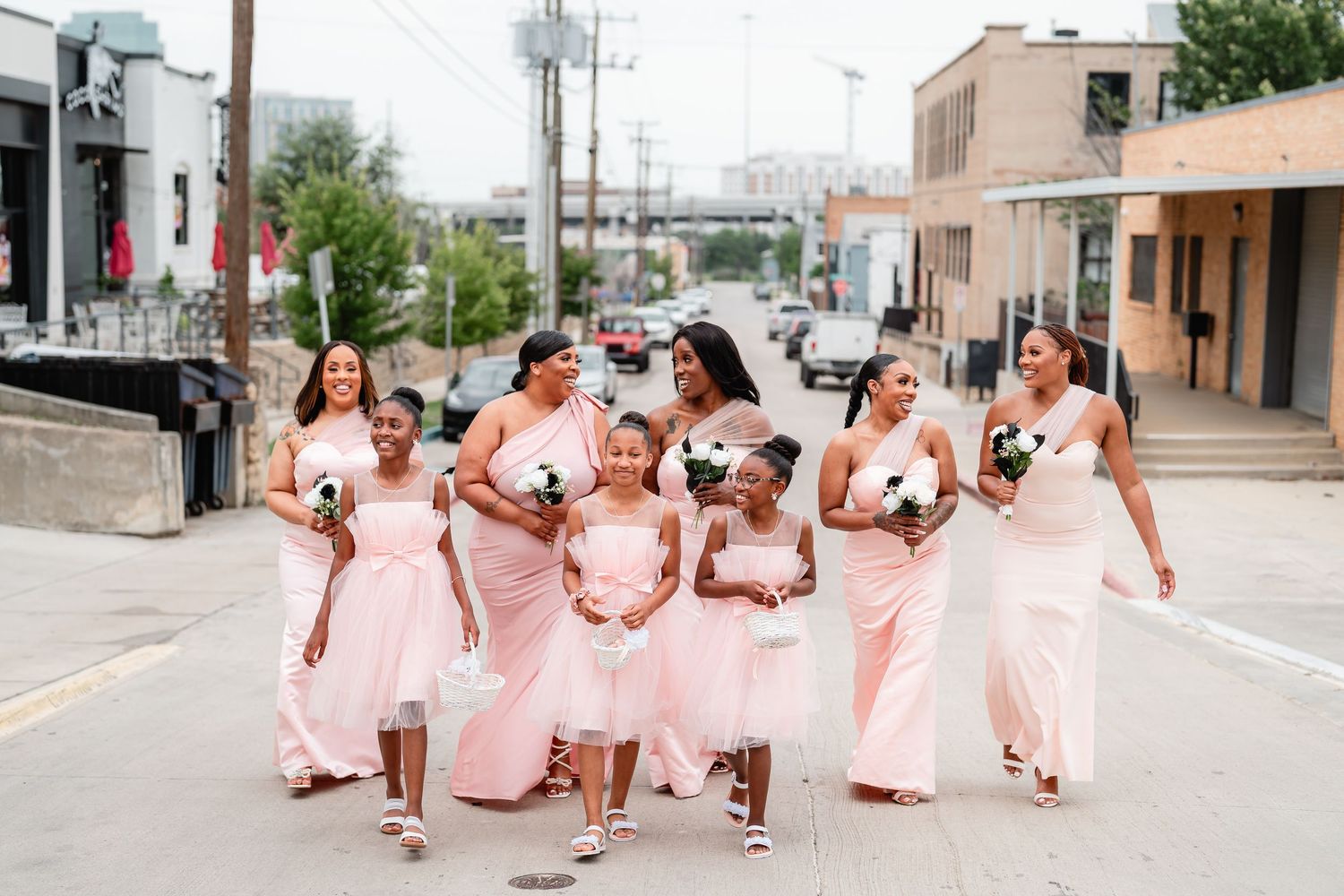 A group in pink dresses walking together down a city street while holding bouquets.