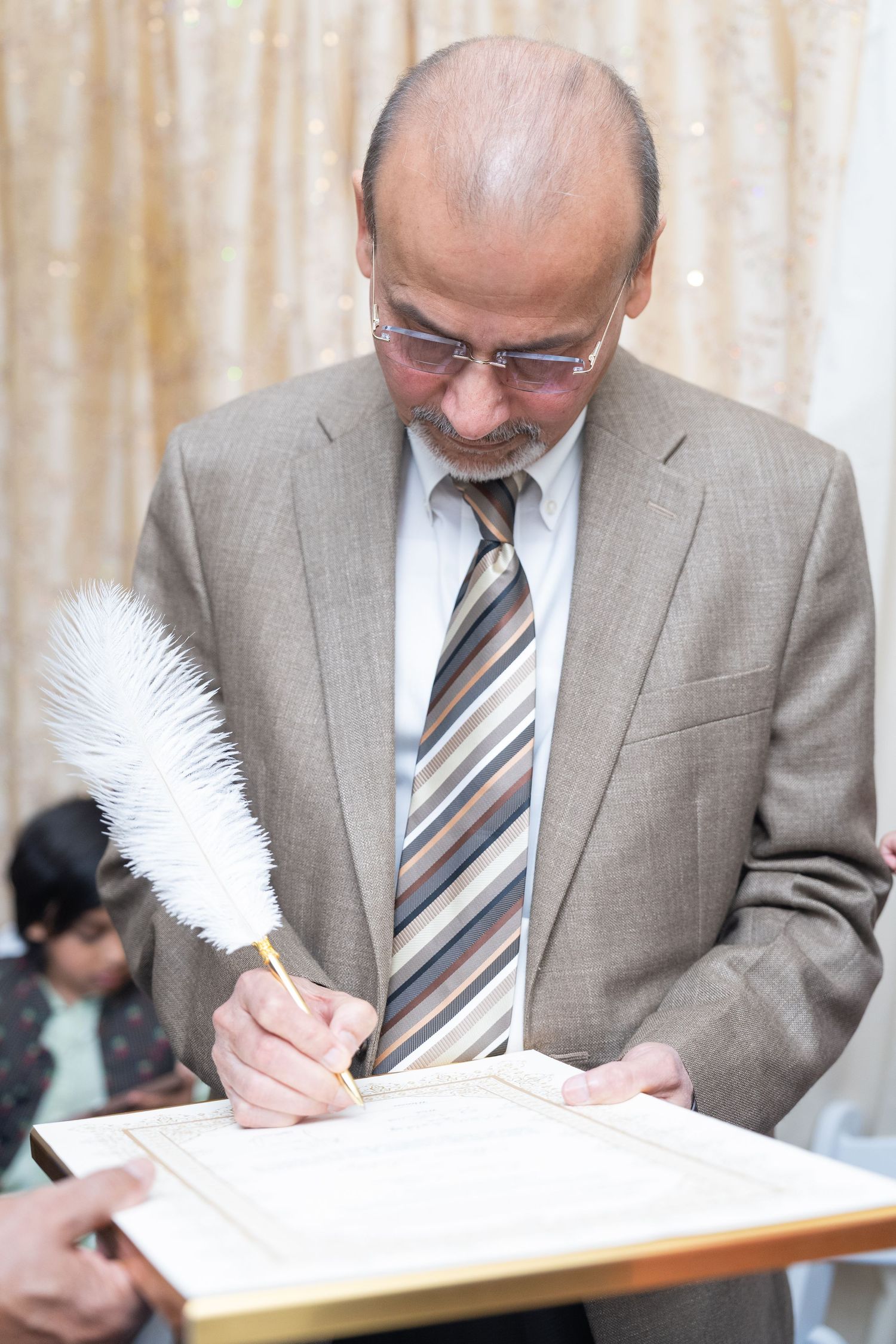 Person in a gray suit signing a document with a white feather quill pen.