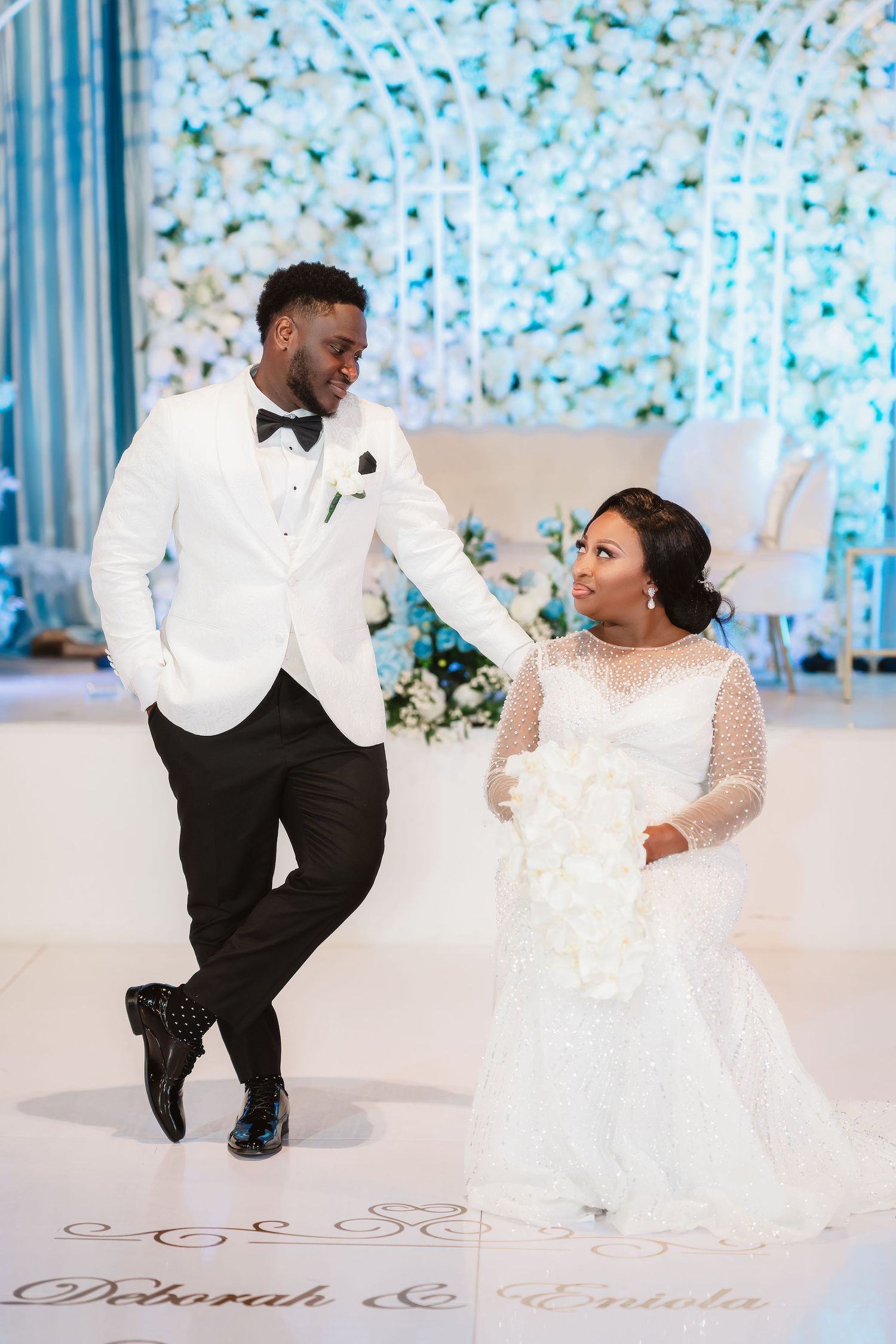 A joyful couple shares a dance moment at their wedding reception against a blue floral backdrop.