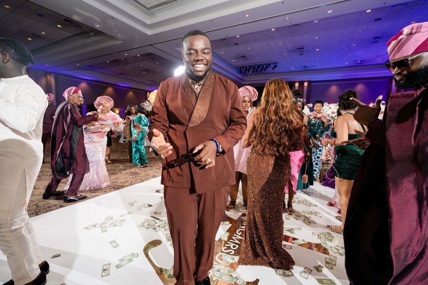 Wedding guests gather on the dance floor during a reception with purple and pink lighting effects.